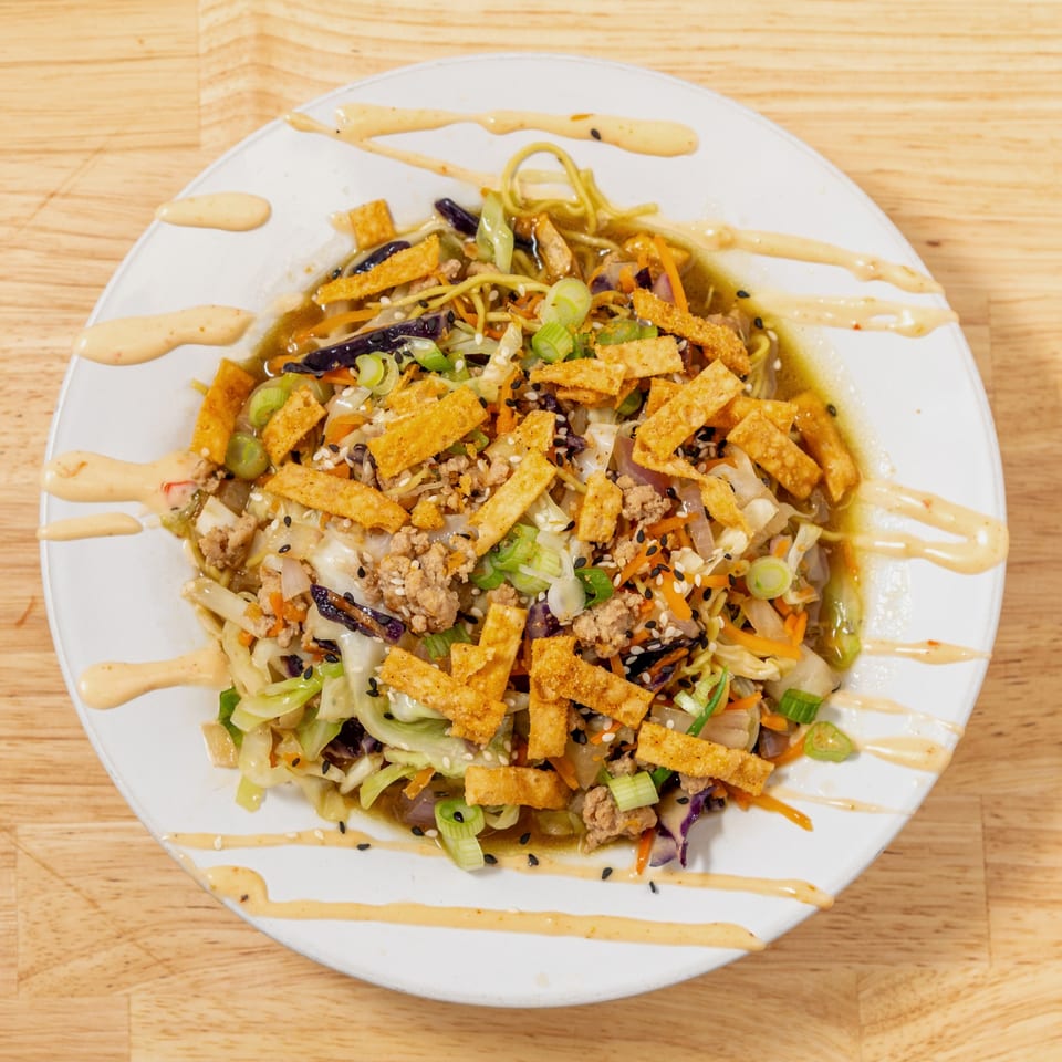 Egg roll bowl with noodles, ground meat, vegetables, crispy wontons, and a creamy sauce.