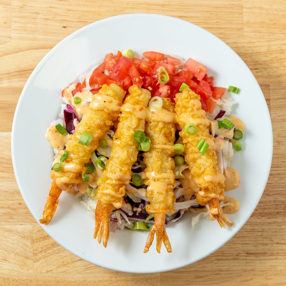 Four crispy fried shrimp with sauce, green onions, and diced tomatoes on a bed of shredded cabbage.