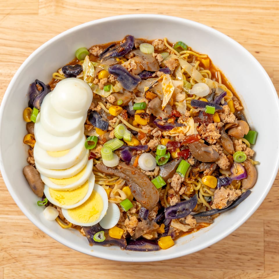 A bowl of ramen with noodles, ground meat, vegetables, and sliced hard-boiled eggs.