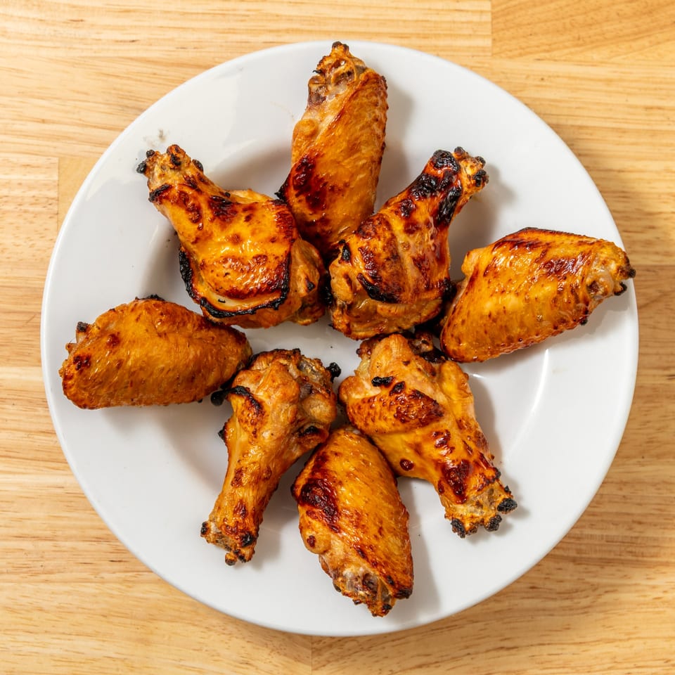 Eight golden-brown chicken wings with crispy skin arranged in a circle on a white plate.